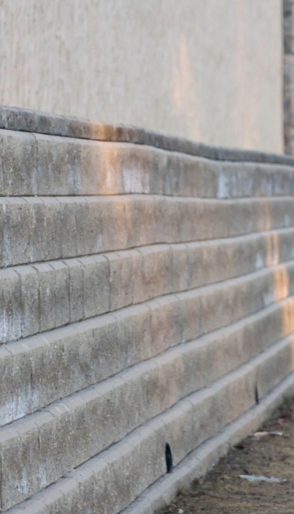 Concrete block retaining wall with stepped courses and visible drainage outlets